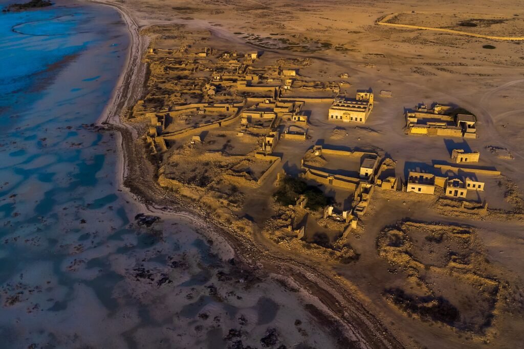 Aerial view of the ruined coral-stone houses of Al Jumail fishing village beside the shoreline