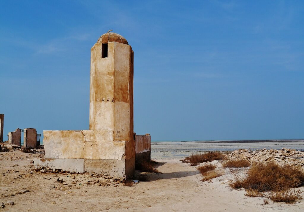 Weathered minaret of the old mosque at Al Khuwayr against a deep blue sky