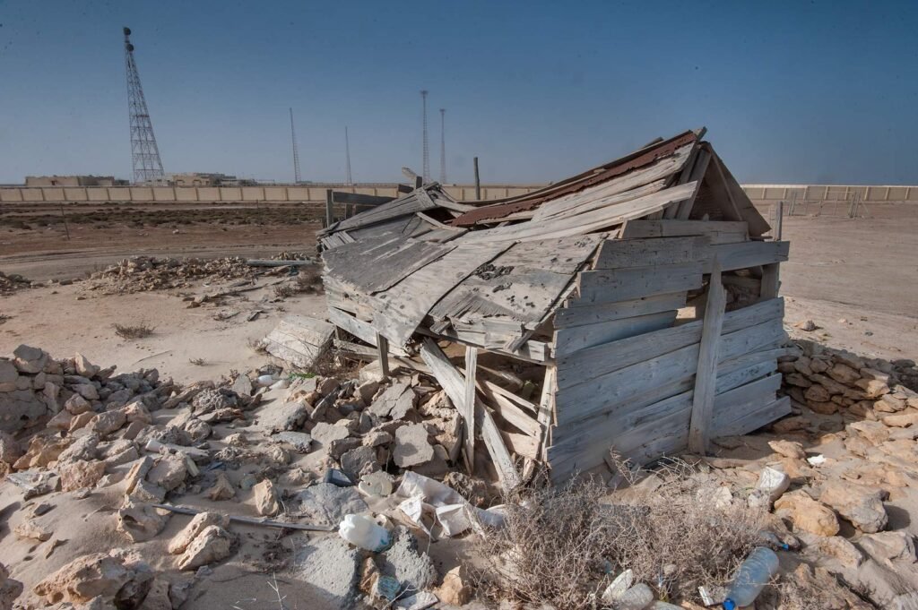 A collapsing wooden building among rubble at Al Khuwayr