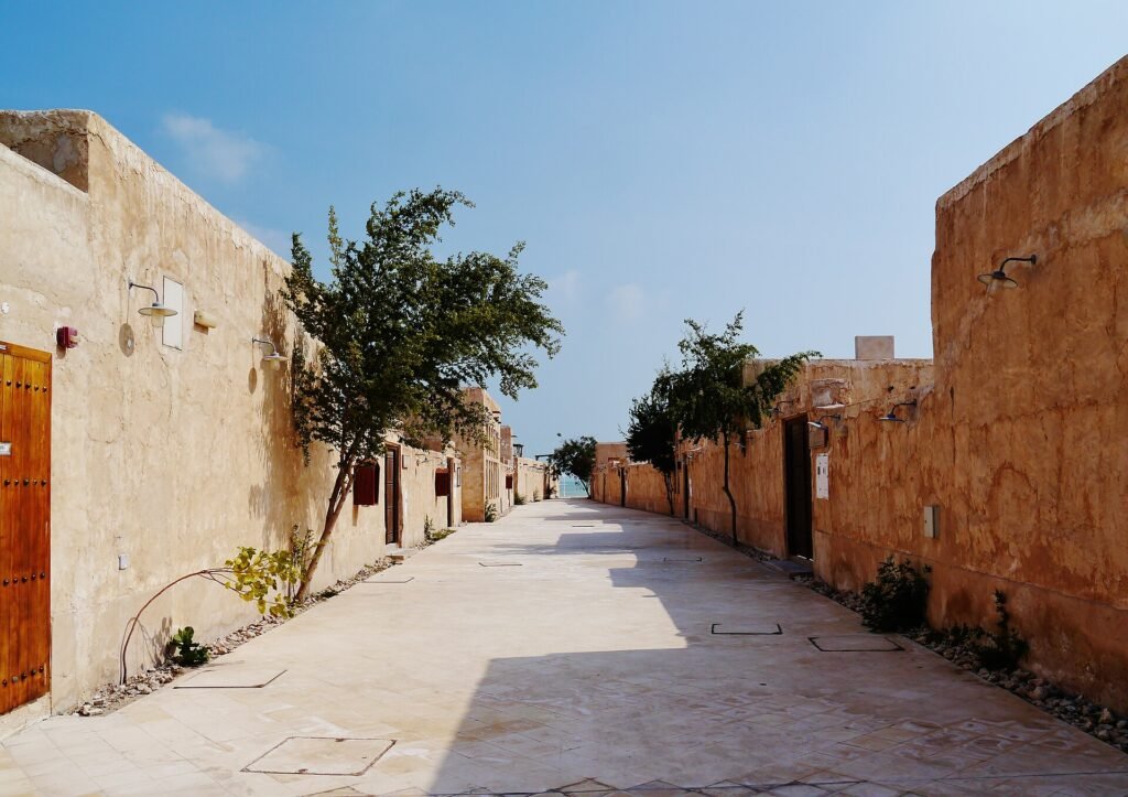 A quiet lane between clay-coloured walls and trees in Souq Al Wakrah