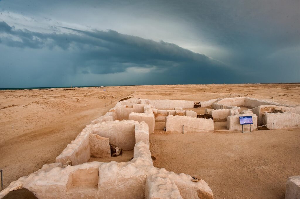 Excavated coral-stone house walls in the ruined town of Al Zubarah under storm clouds