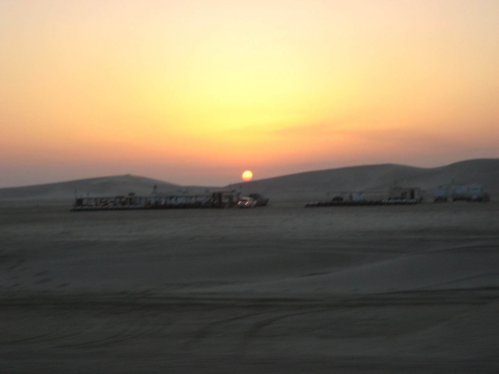 Sun dropping behind low dunes on the road to Sealine near Mesaieed