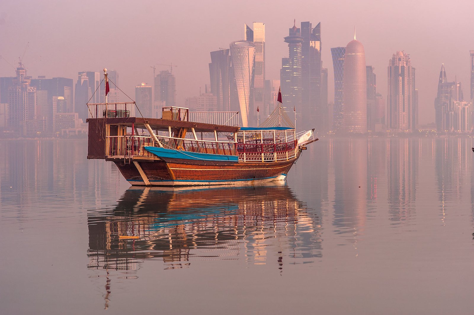 A dhow on calm water in Doha Bay with the West Bay towers in morning haze
