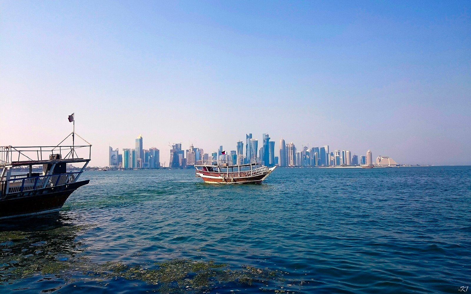 Wooden dhow crossing Doha Bay with the West Bay skyline behind, seen from the Corniche