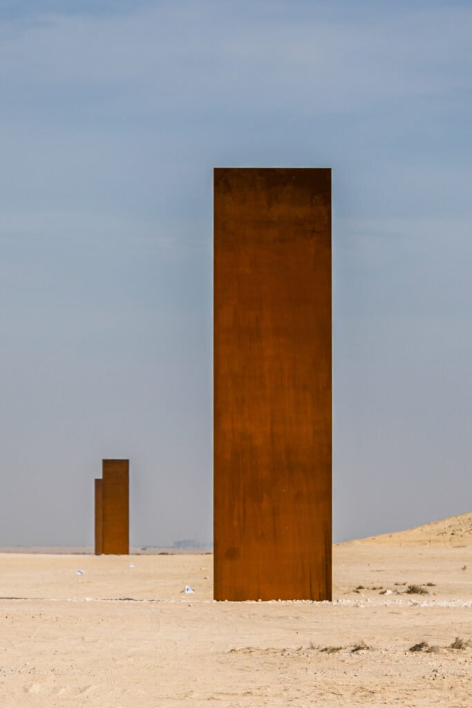 Looking up at a rusted steel plate of East-West/West-East with a second plate in the distance