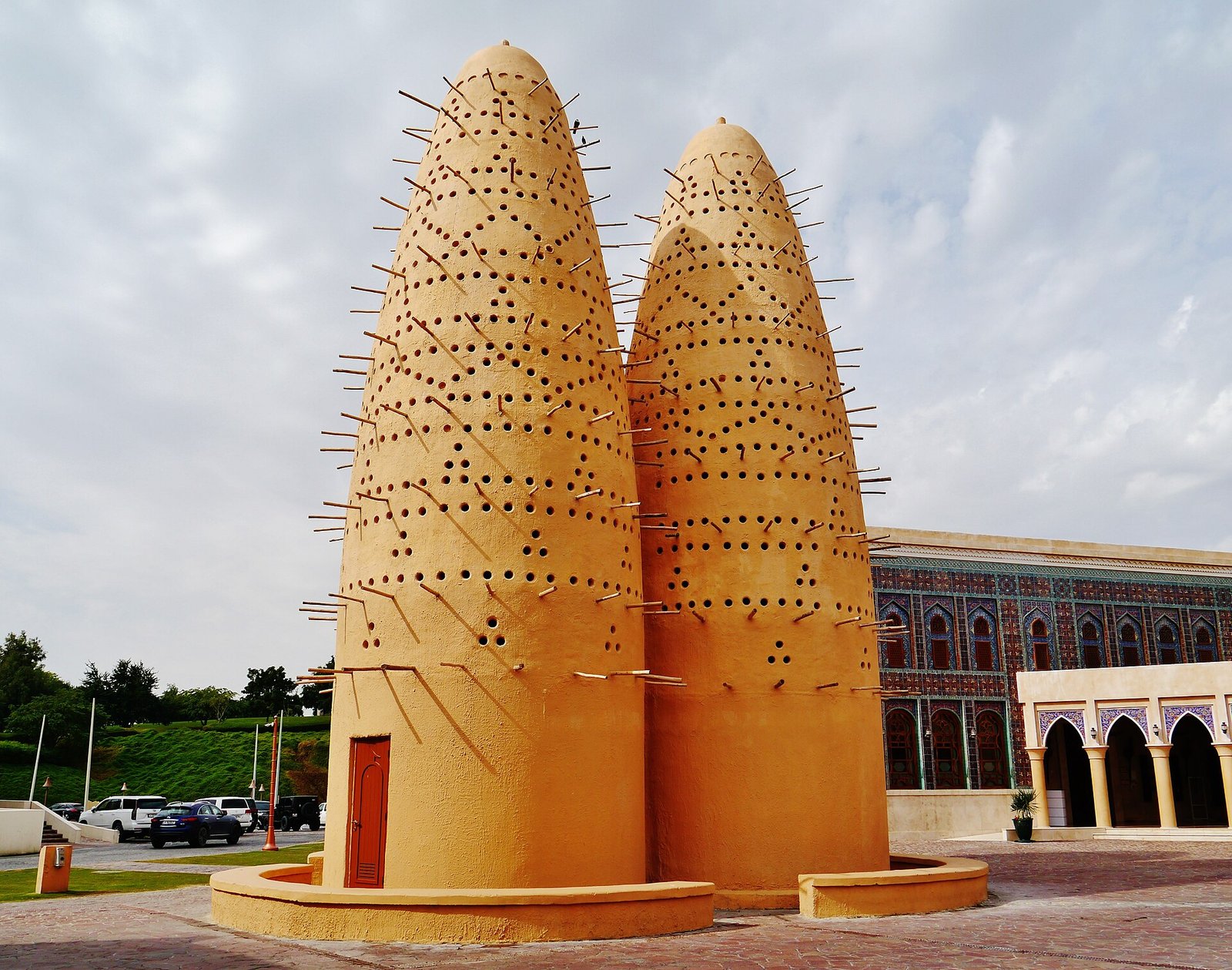 Two pigeon towers on a paved plaza in front of a Katara building with arches