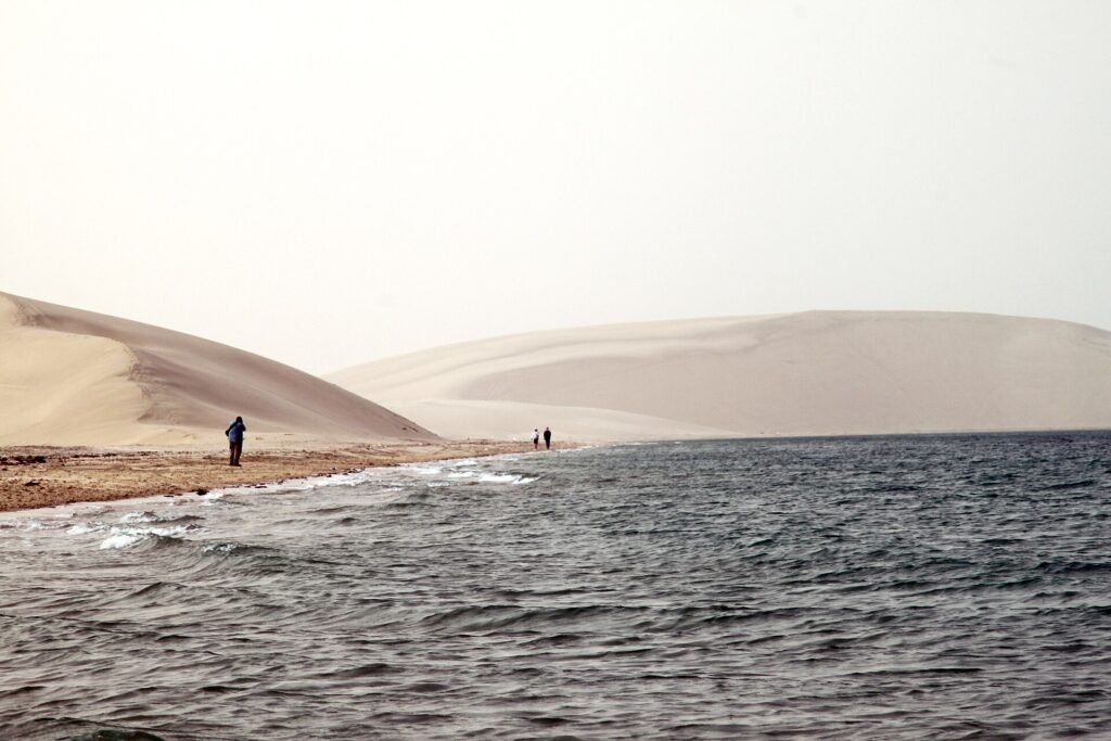 Visitors standing where the sand dunes meet the shallow water of Qatar's Inland Sea