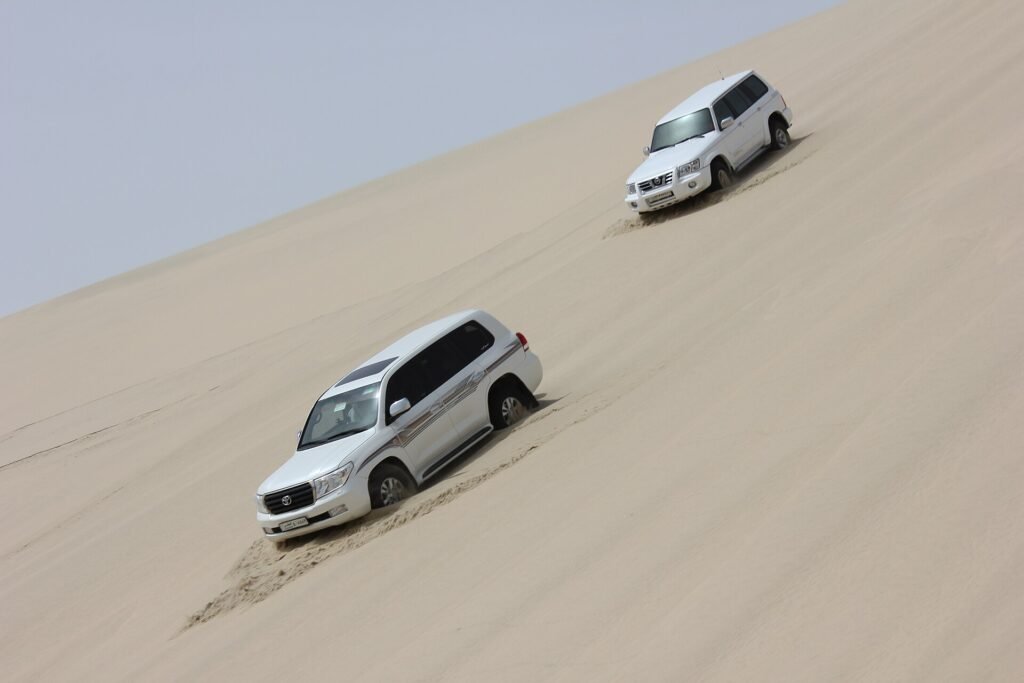 Two 4x4 vehicles driving down a steep sand dune on the way to the Inland Sea, Qatar