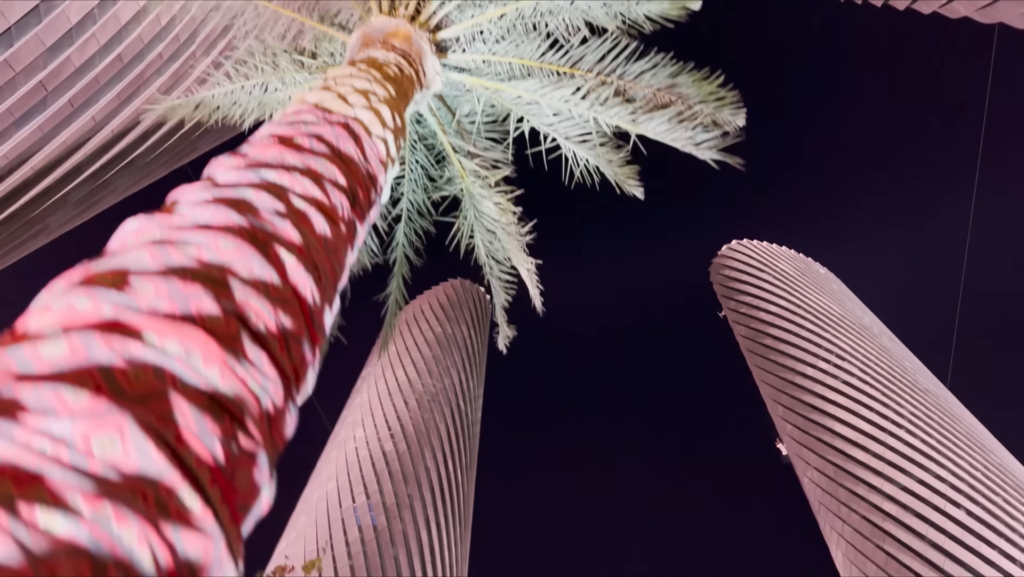 Looking up at the Lusail Plaza Towers past a palm tree on Lusail Boulevard at night