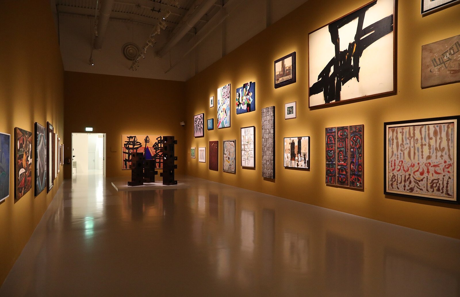 Paintings hung in a warmly lit exhibition gallery at Mathaf, Doha