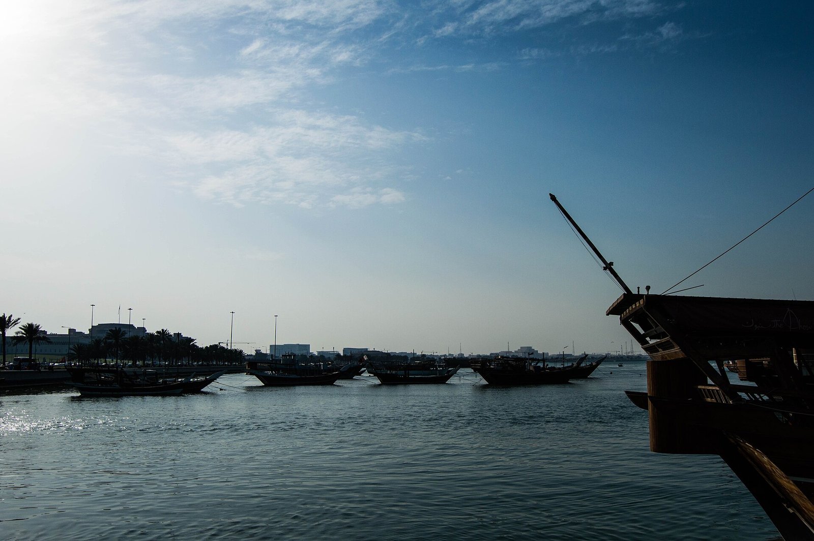 A dhow bow and moored boats silhouetted in the harbour at Old Doha Port
