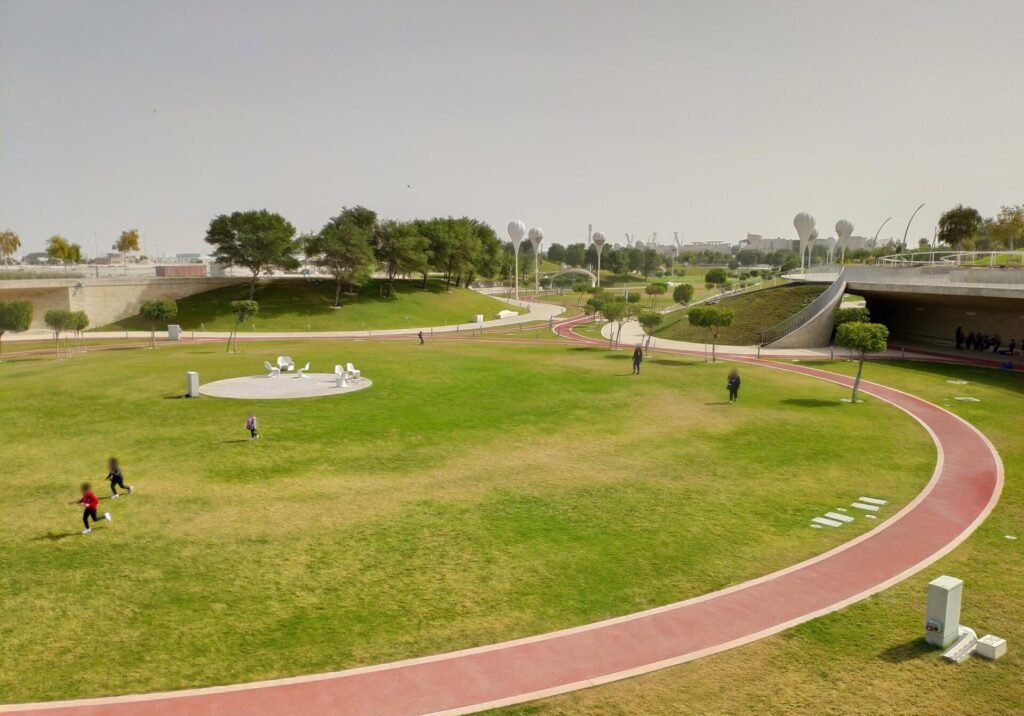 Red running track curving around grassy mounds at Oxygen Park, Education City
