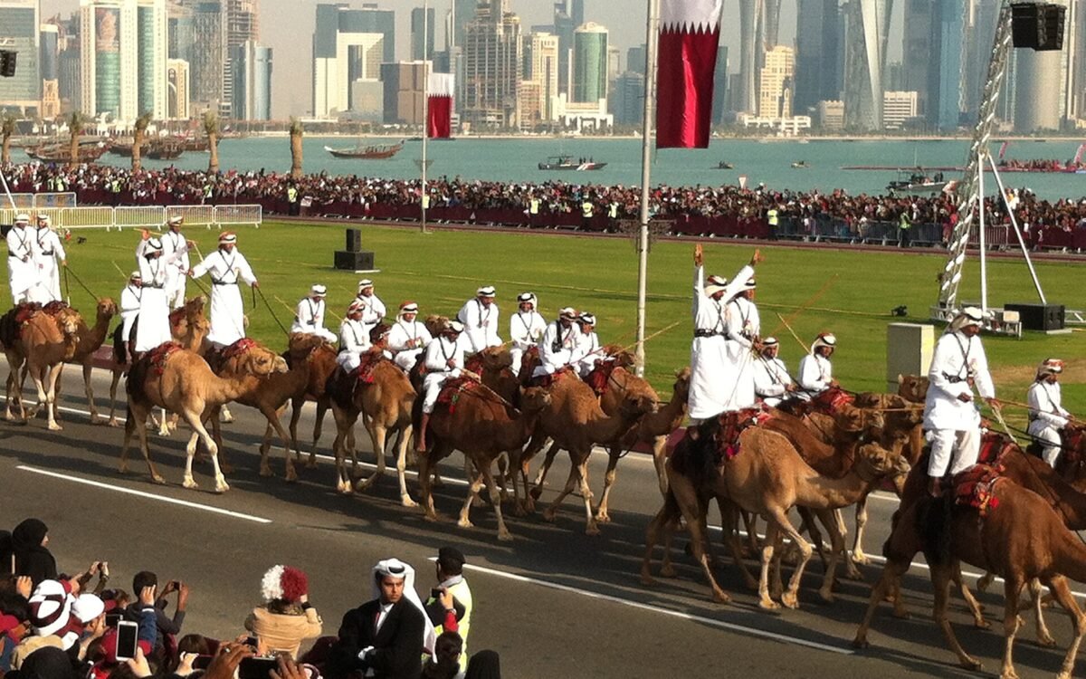 Camel riders in white thobes parade along the Doha Corniche on Qatar National Day with the West Bay skyline behind