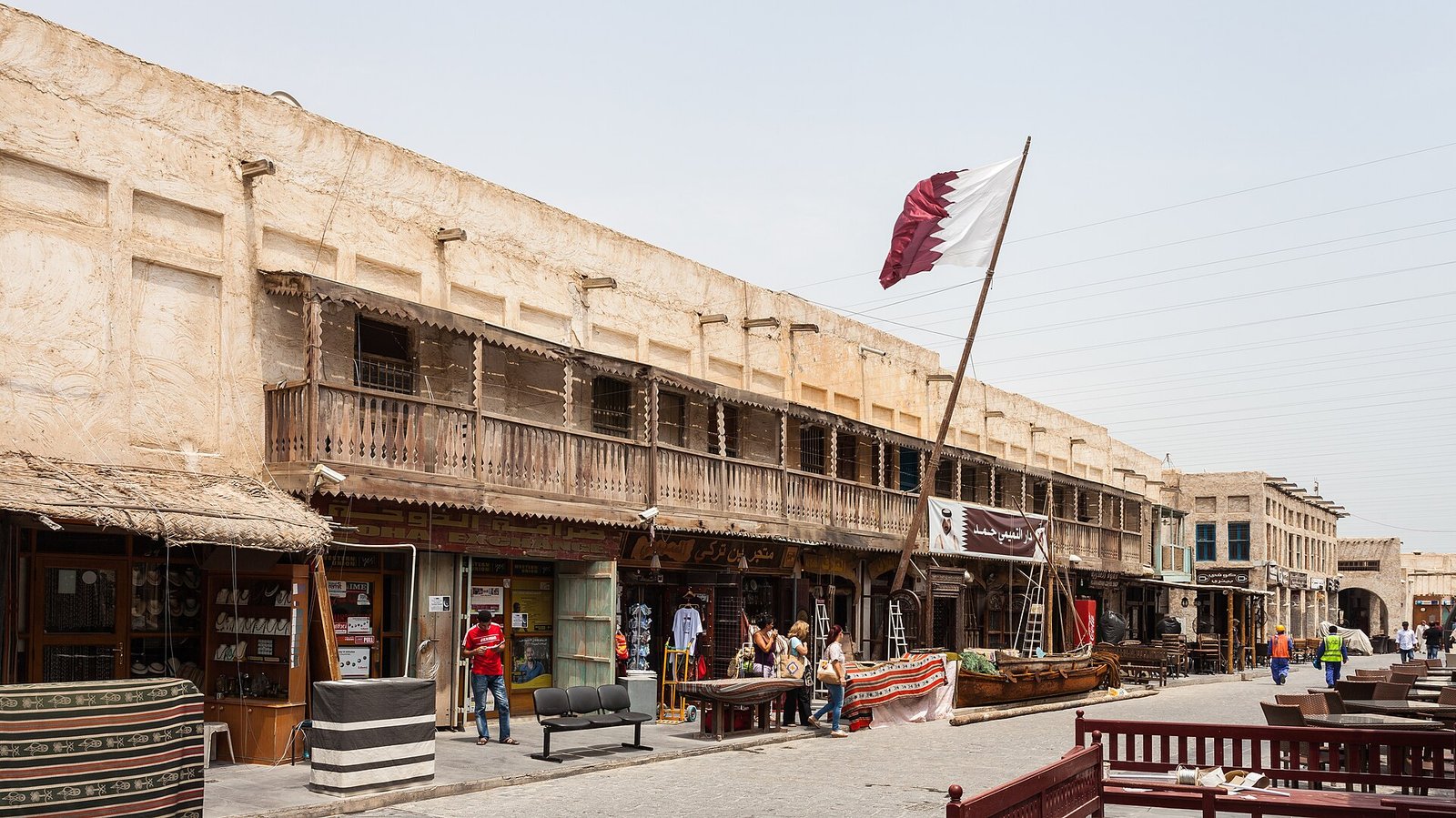 Wooden balconies and shopfronts along a main lane of Souq Waqif with a Qatari flag