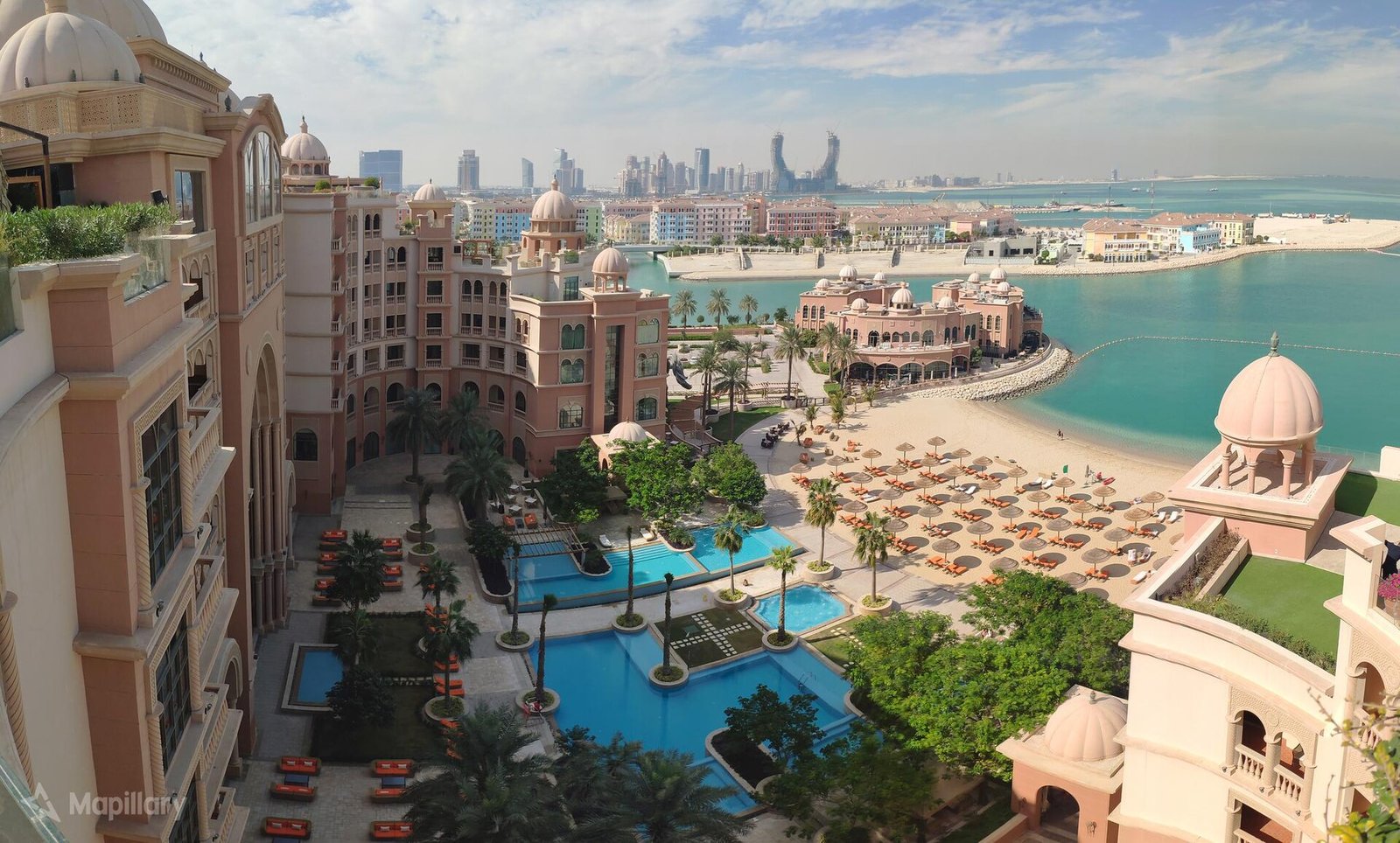 Pools, sunbeds and a sandy beach on The Pearl-Qatar seen from above, with towers in the distance