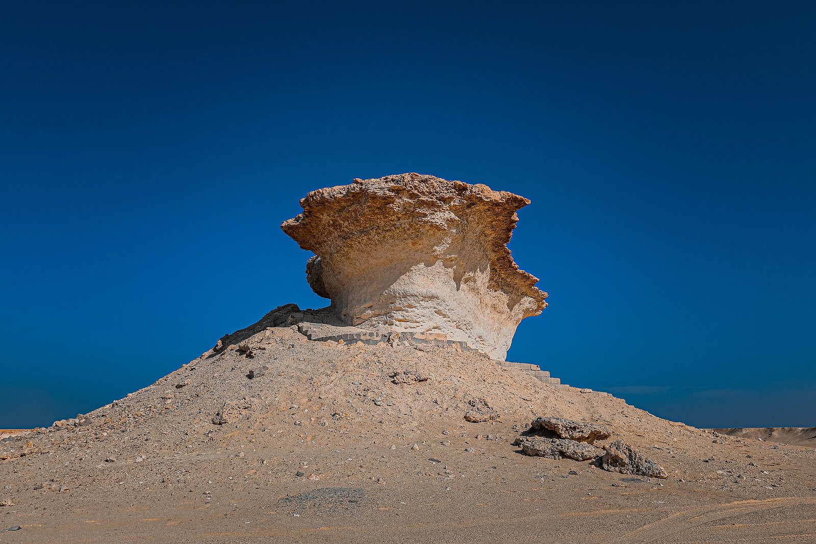 Wind-eroded limestone mushroom rock on a pale mound against a deep blue sky, Zekreet Peninsula