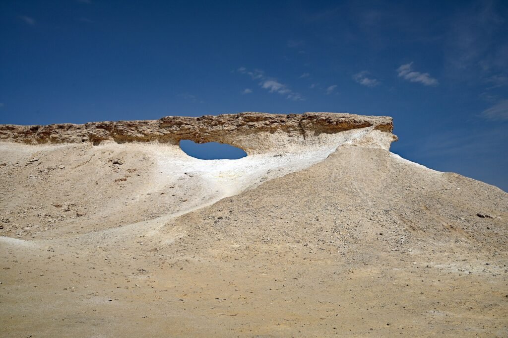 Flat limestone cap with a natural window on a white chalky mound, Zekreet Peninsula